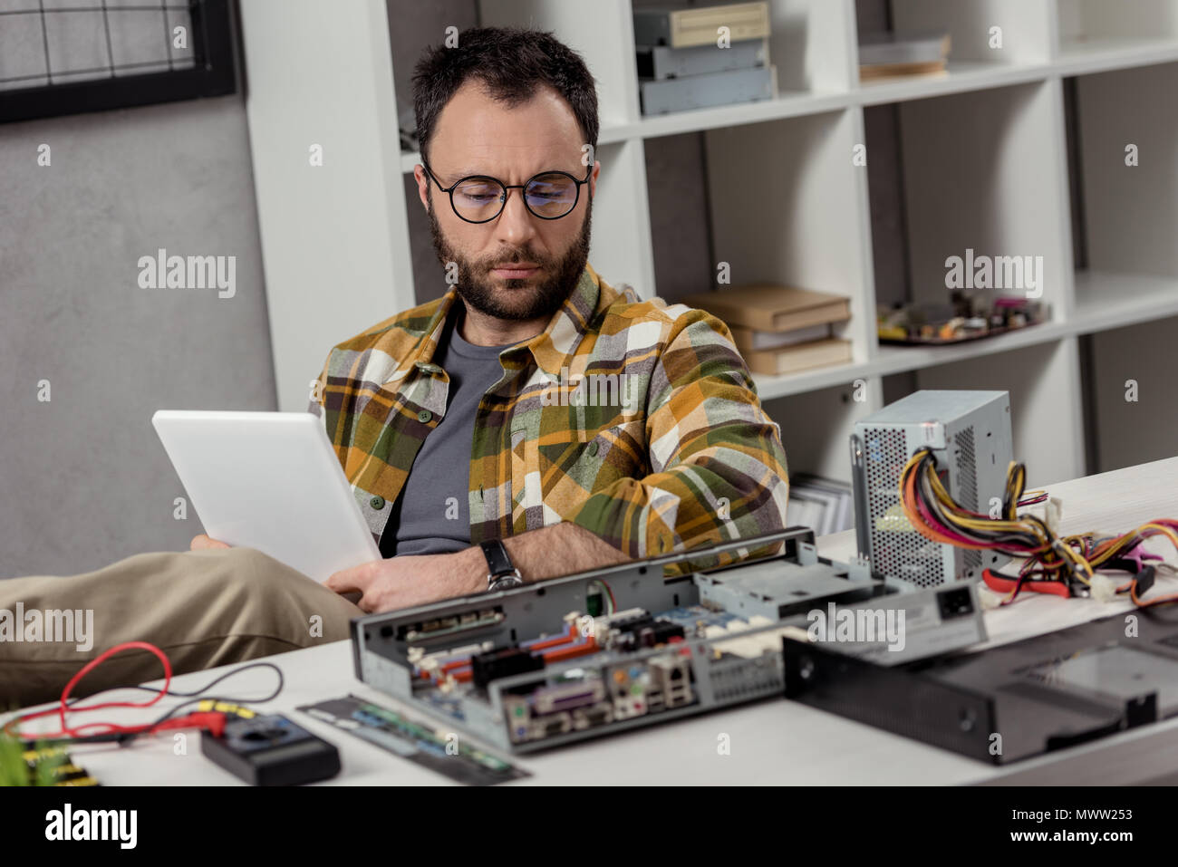 man using digital tablet while sitting against broken pc on table Stock Photo