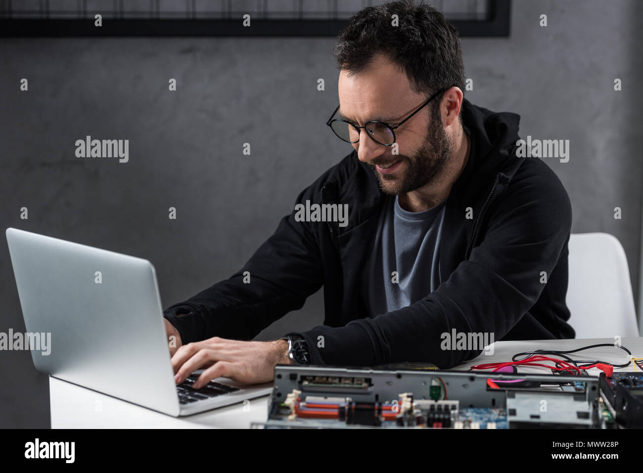 smiling man using laptop against broken pc on table Stock Photo