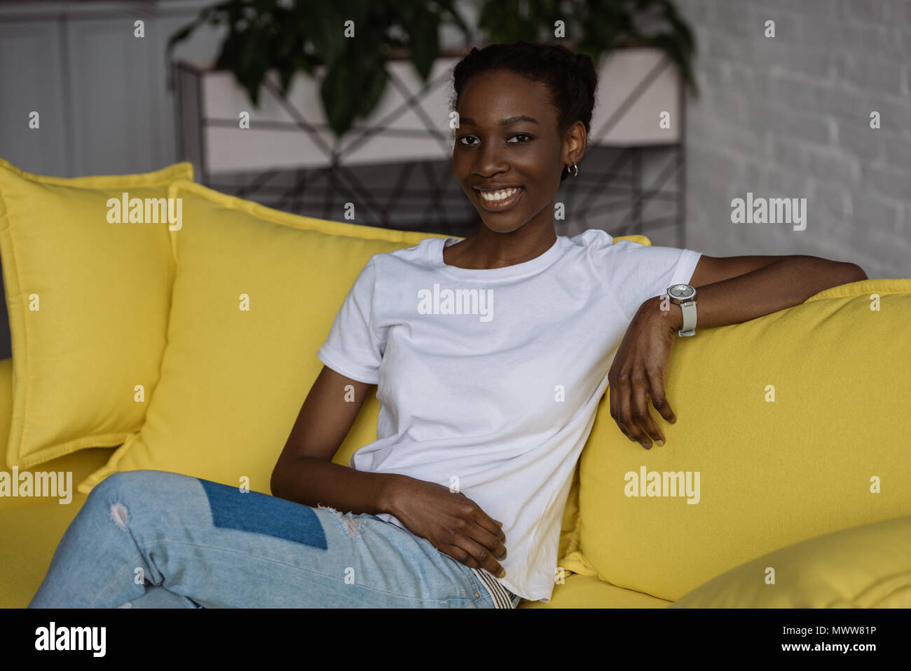 beautiful african american girl sitting on yellow couch and smiling at ...