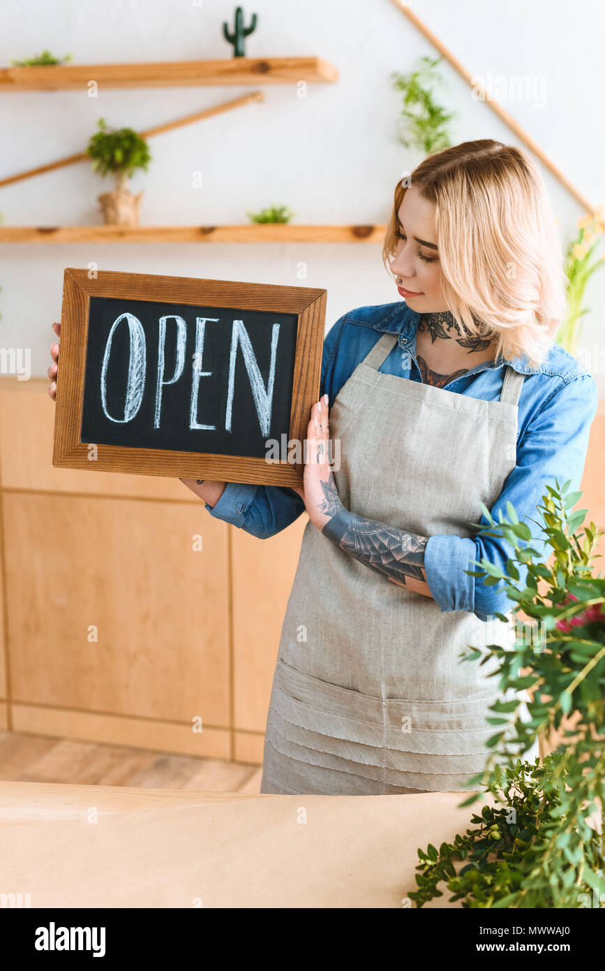 beautiful young woman in apron holding sign open in flower shop Stock Photo