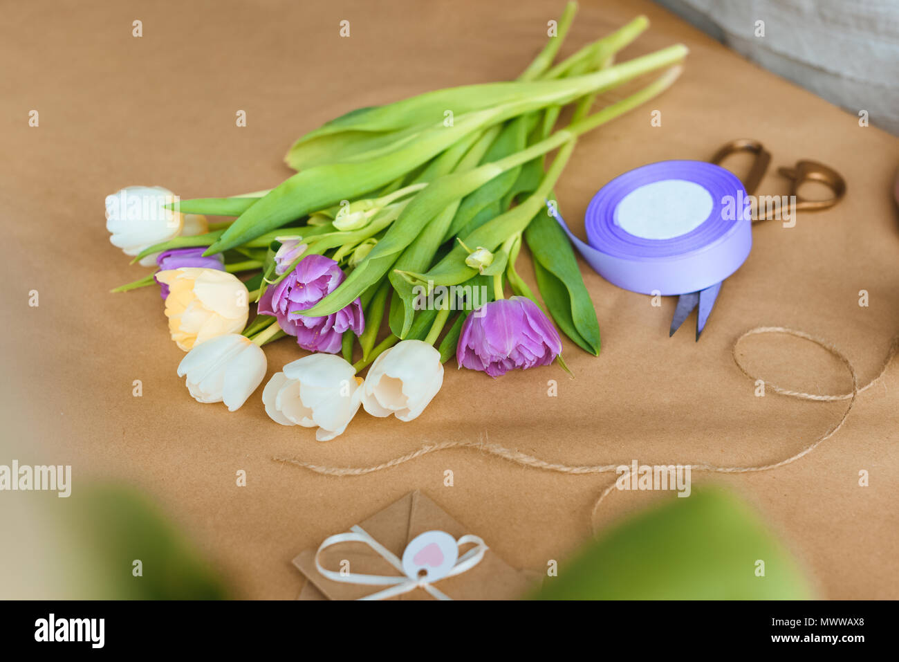 close-up view of beautiful tender tulips, rope, ribbon and scissors on craft paper Stock Photo