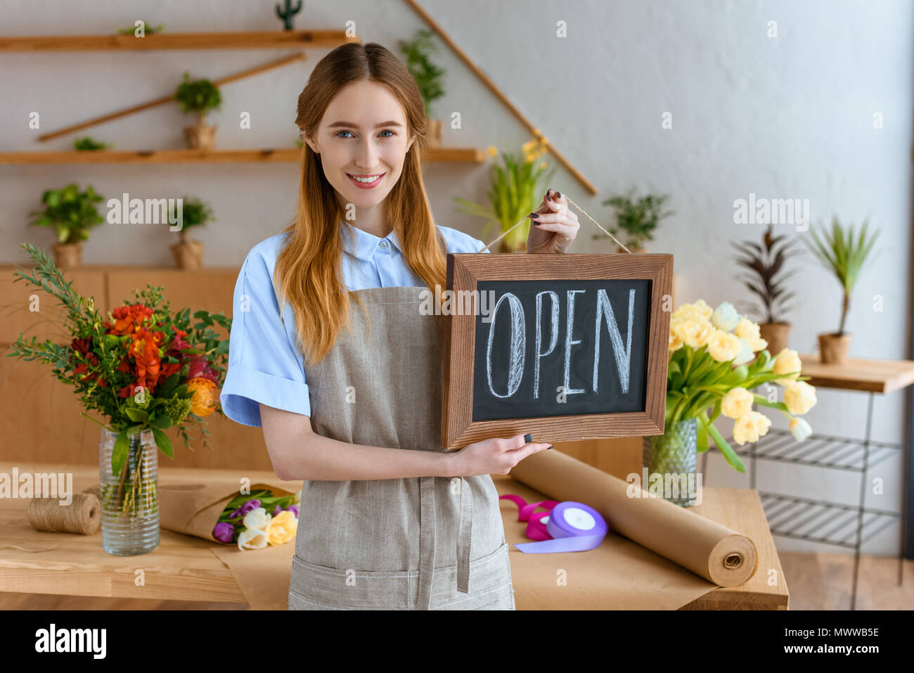 beautiful young florist holding sign open and smiling at camera in flower shop Stock Photo