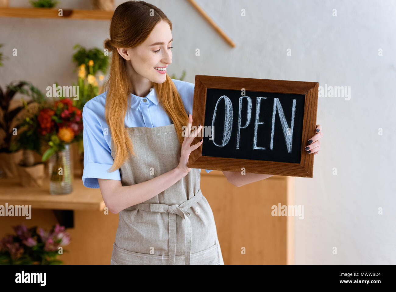 beautiful smiling young florist holding sign open in flower shop Stock Photo