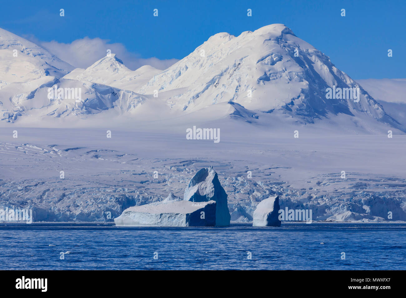 Non-tabular iceberg off glaciated, mountainous Anvers Island, blue sky, Antarctic Peninsula, Antarctica, Polar Regions Stock Photo