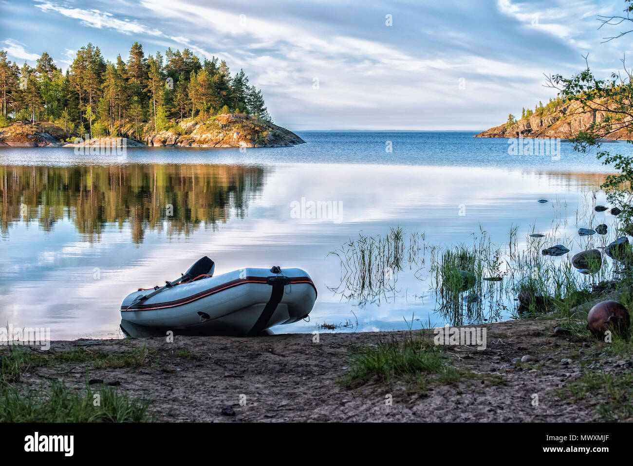 Morning at the uninhabited wild beach. Empty inflatable boat with motor and oars at the coastline. Summer season. Selective focus. Active tourism conc Stock Photo