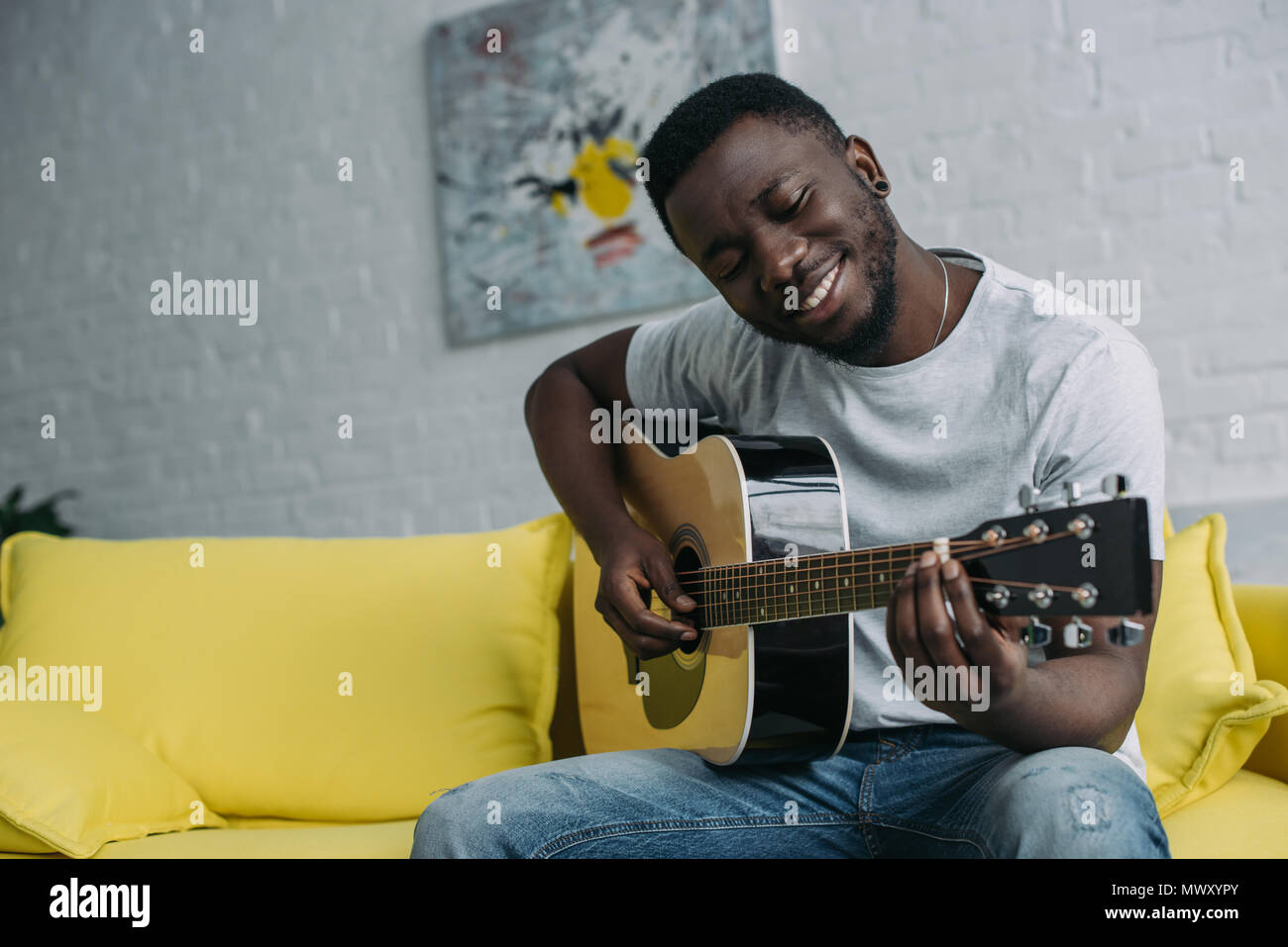 handsome smiling young african american man playing guitar at home ...