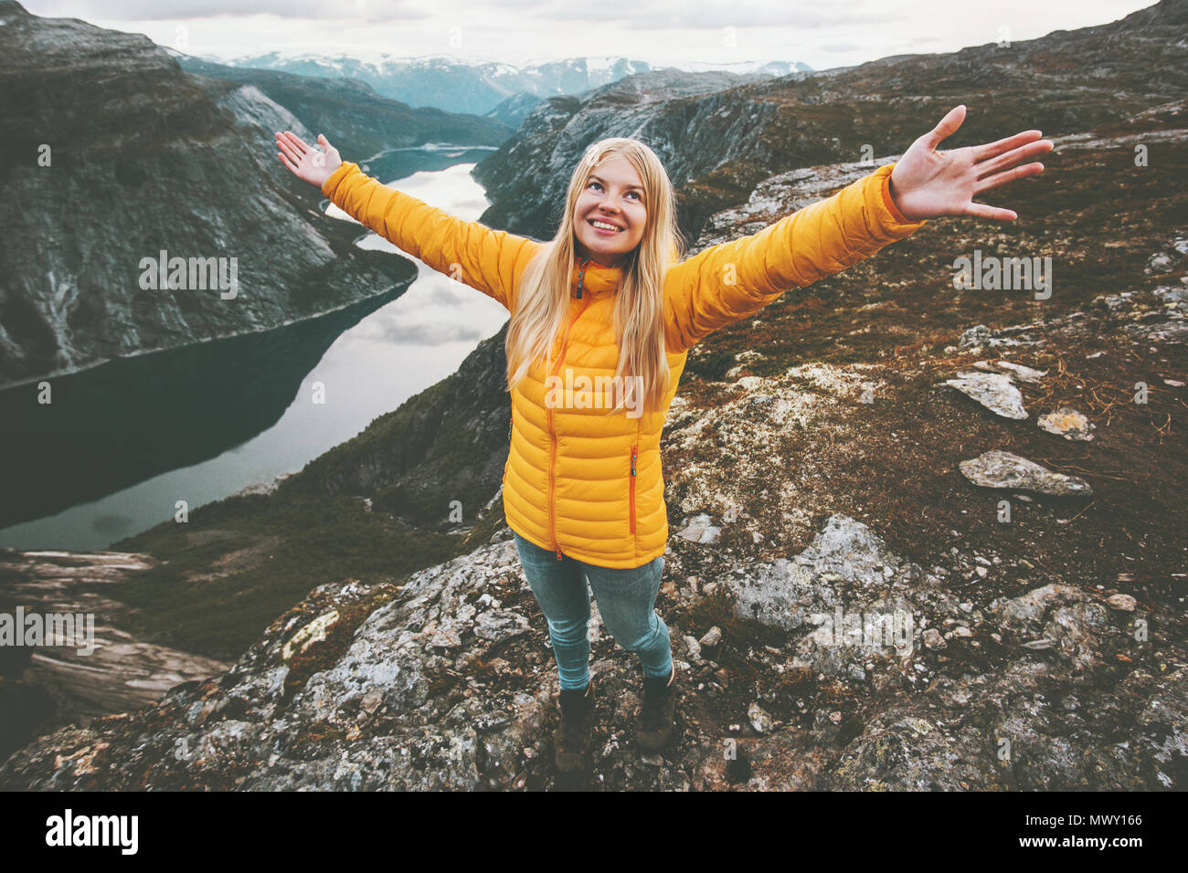Happy girl success raised hands standing on mountain summit hiking travel adventure lifestyle vacations weekend getaway aerial  lake landscape in Norw Stock Photo