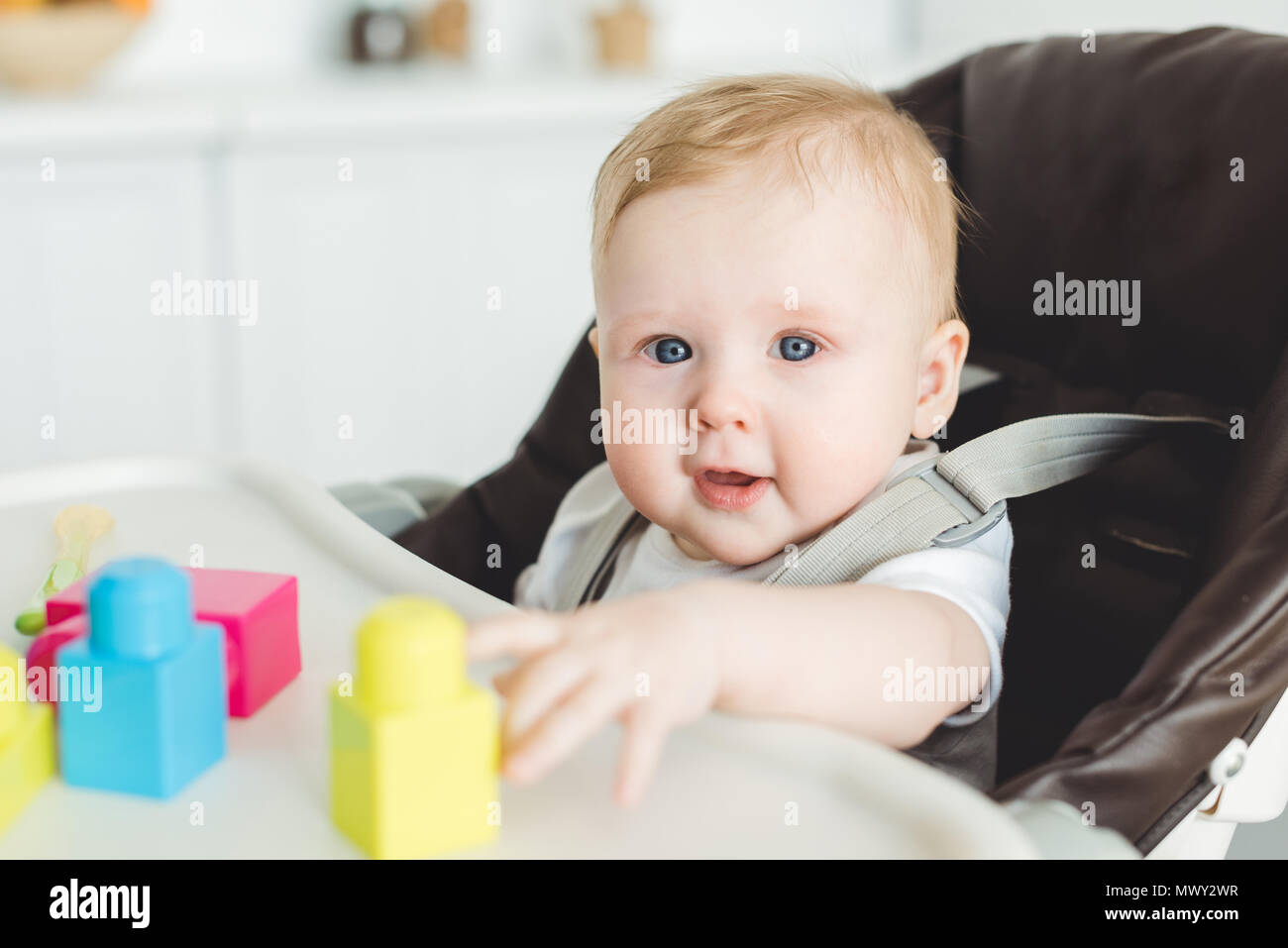 Smiling infant sitting in baby chair and playing with plastic blocks Stock Photo
