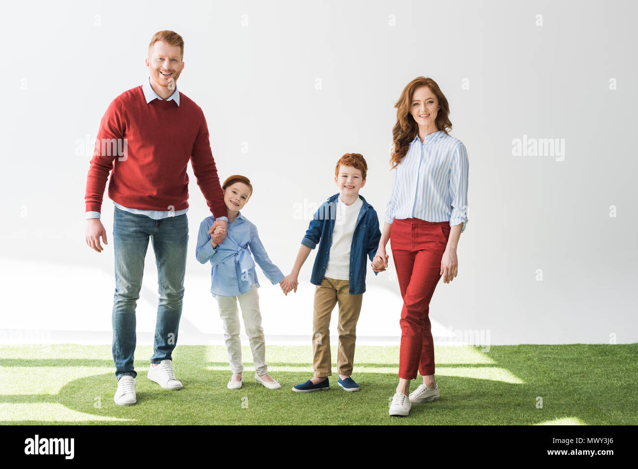 happy redhead family with two children holding hands and smiling at camera on grey Stock Photo