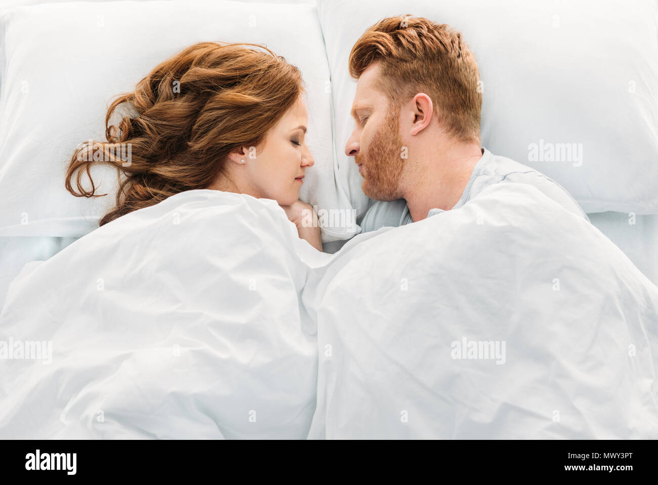 top view of beautiful redhead couple sleeping face to face in bed Stock