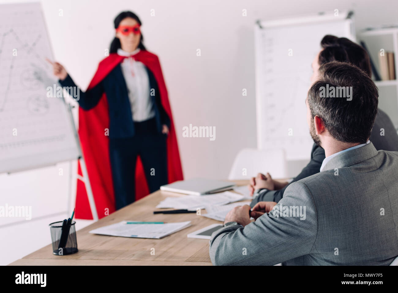 super businesswoman in mask and cape showing presentation for businessman in office Stock Photo