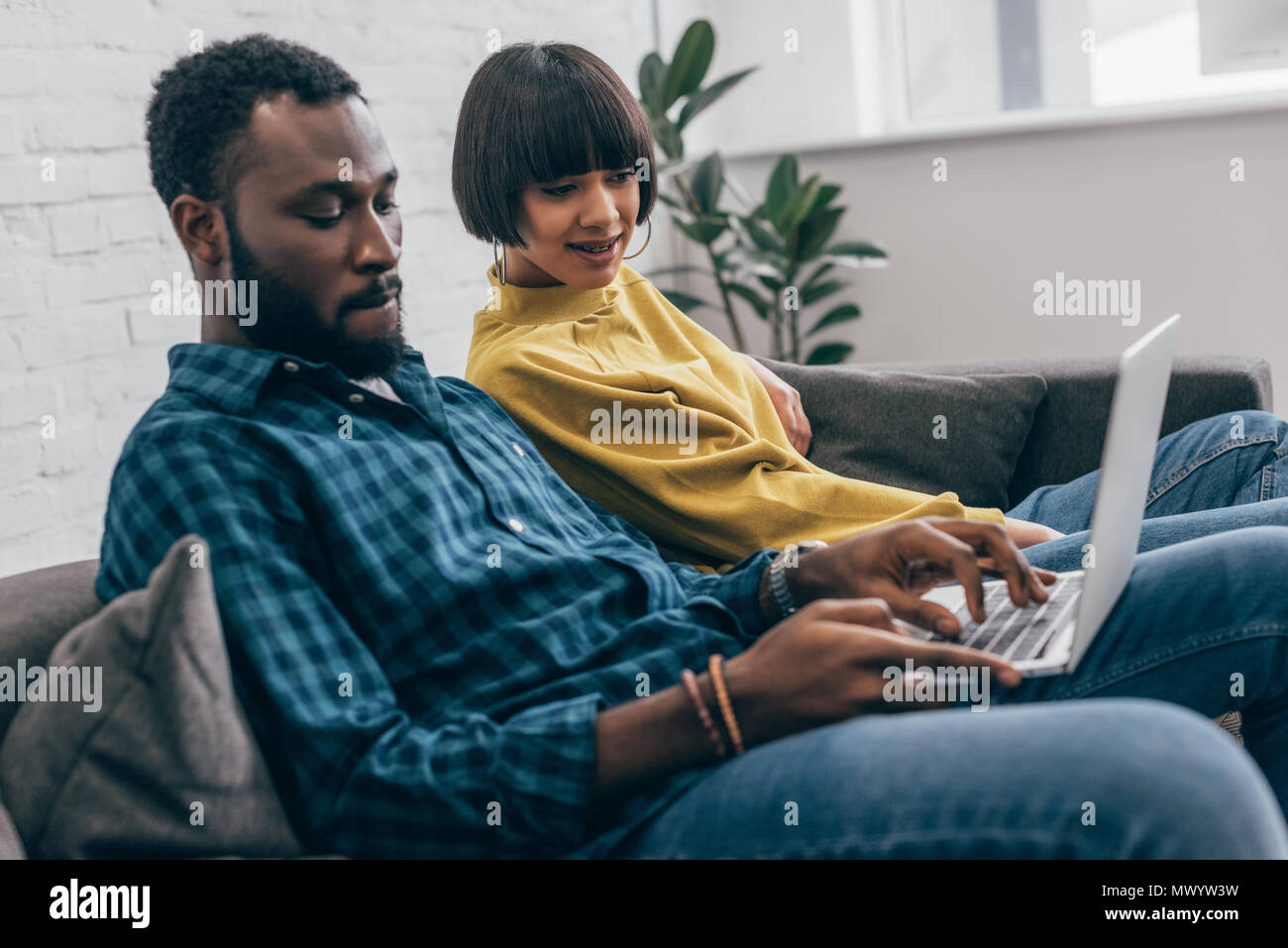 african american young man typing on laptop and his girlfriend watching ...