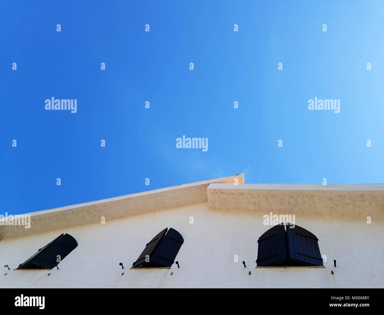 roof of white house with wooden brown windows against blue sky Stock