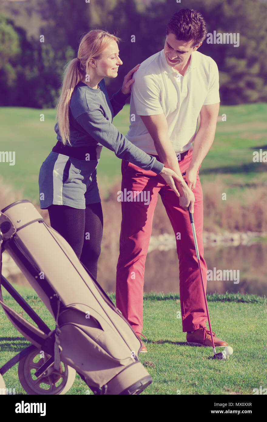 Happy golf trainer showing male player how to hit ball rightly Stock
