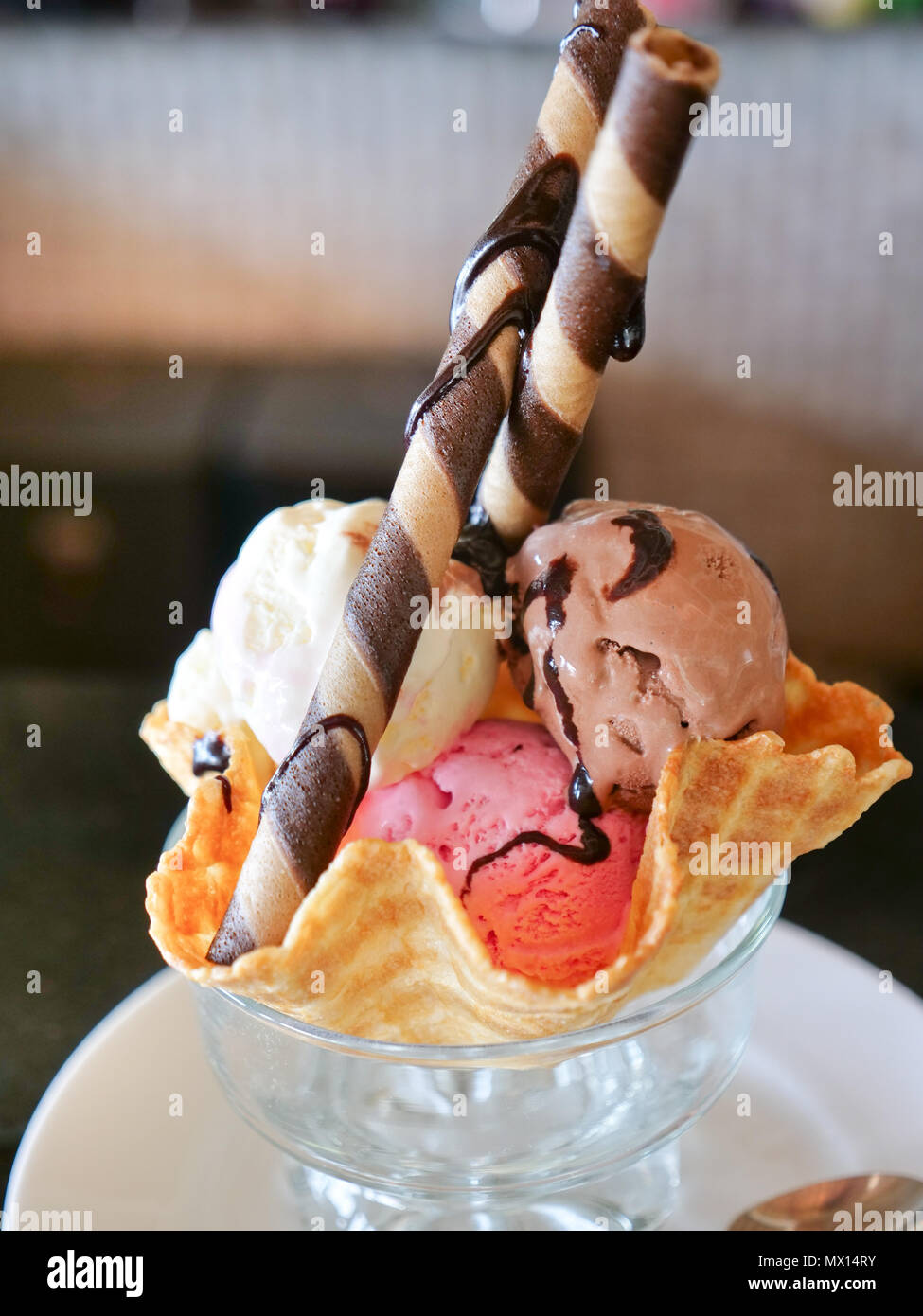 Mixed ice cream scoops in wafer bowl. Dessert Sundae with Neapolitan Flavors of Ice Cream - Glass Dish with Scoops of Chocolate, Vanilla, and Strawberry Ice Cream with Rolled Cookie Biscuits and Garnishes Stock Photo