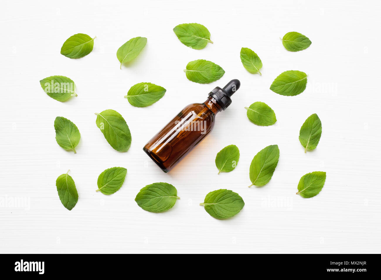 Mint Essential Oil in a Glass Bottle with leaves on white background
