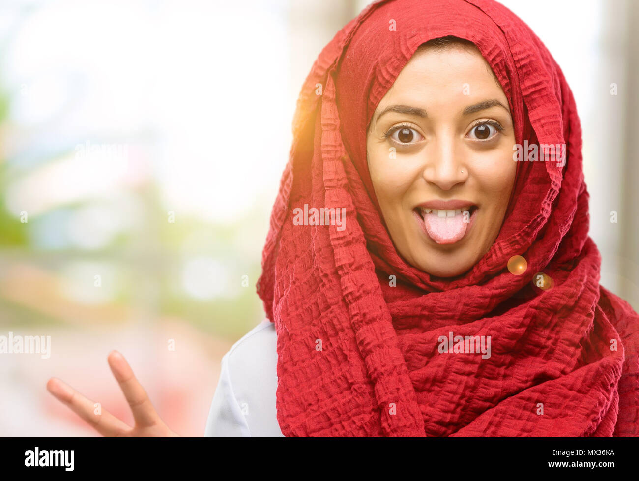 Young arab woman wearing hijab looking at camera showing tong and ...