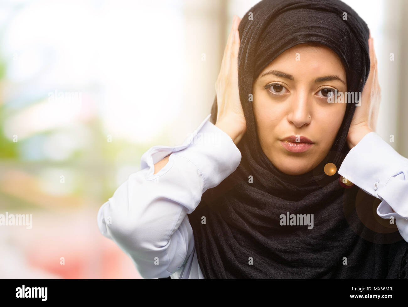 Young arab woman wearing hijab covering ears ignoring annoying loud