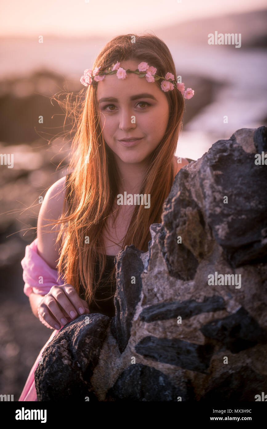 A beautiful female Caucasian model on the California coast during golden hour. Pink accents to the lighting, makeup, and accessories Stock Photo