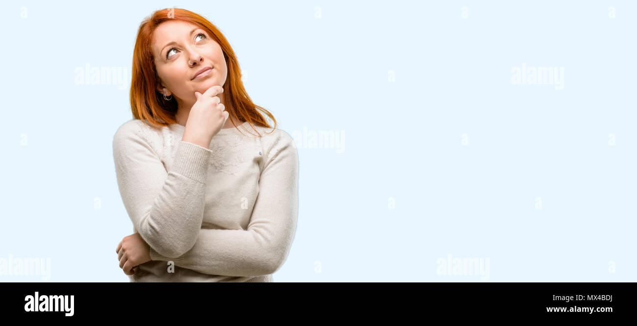 Beautiful young redhead woman thinking and looking up expressing doubt ...