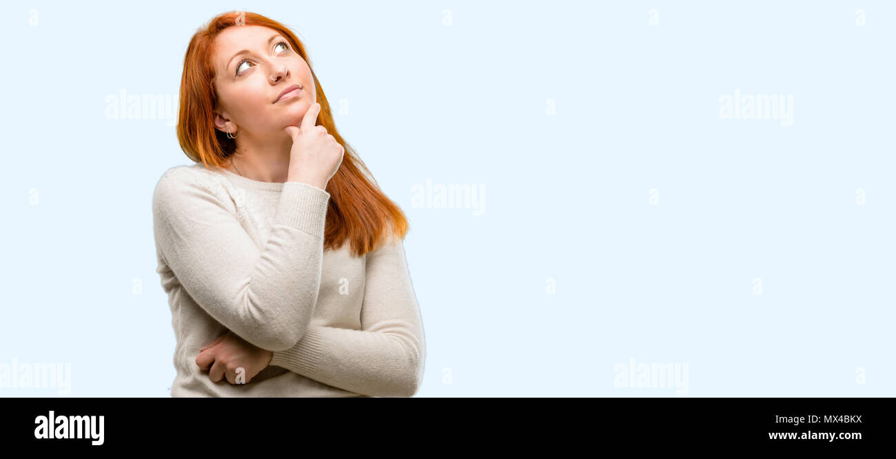 Beautiful young redhead woman thinking and looking up expressing doubt ...