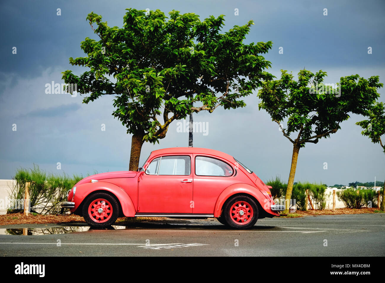 A red VW beetle, lit by the sun against a dark stormy sky Stock Photo