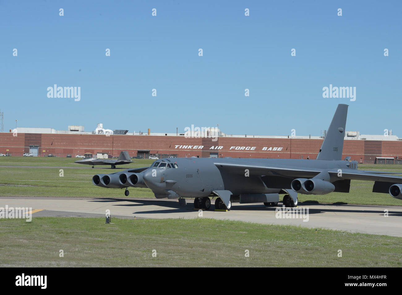 Two vital defense assets are shown together as a Boeing B-52H, 60-0005, poses in front of the  Oklahoma City Air Logistics Complex while a F-22A Raptor of the 325th Fighter Wing, Tyndall Air Force Base, Florida, rolls down the runway on May 1, 2017, Tinker Air Force Base, Oklahoma. OC-ALC is responsible for depot level maintenance of the B-52 fleet as well as overhaul of the Pratt & Whitney F119 engines used in the F-22A. Stock Photo