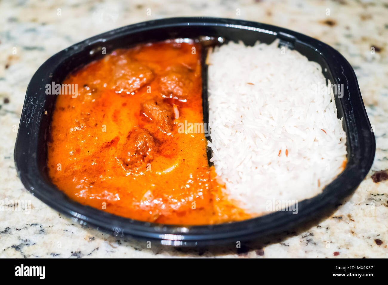 Orange red curry tikka masala sauce macro closeup, with white basmati rice in black plastic tv