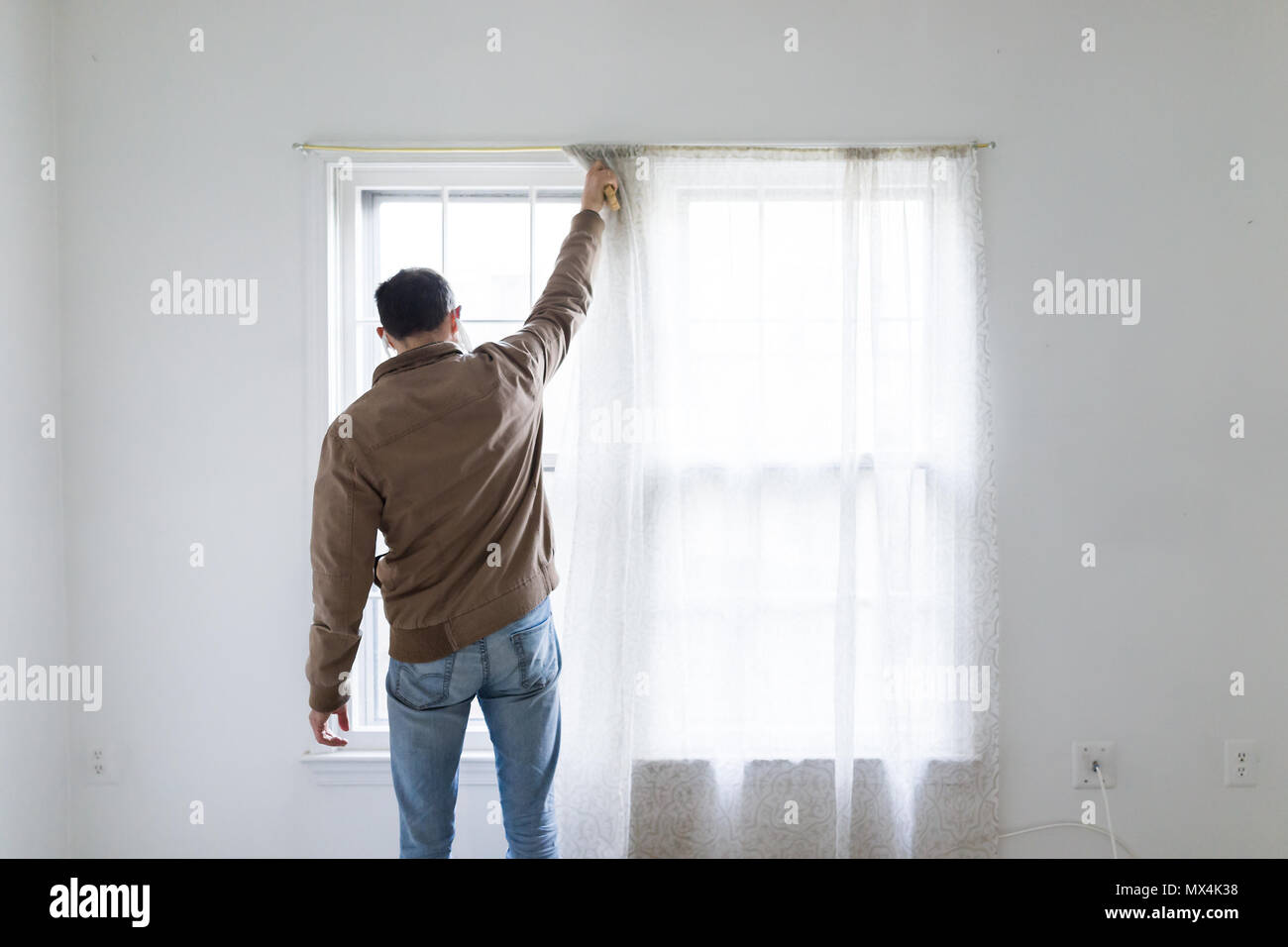 Young Man Standing In Front Of Bright Window In Room Adjusting