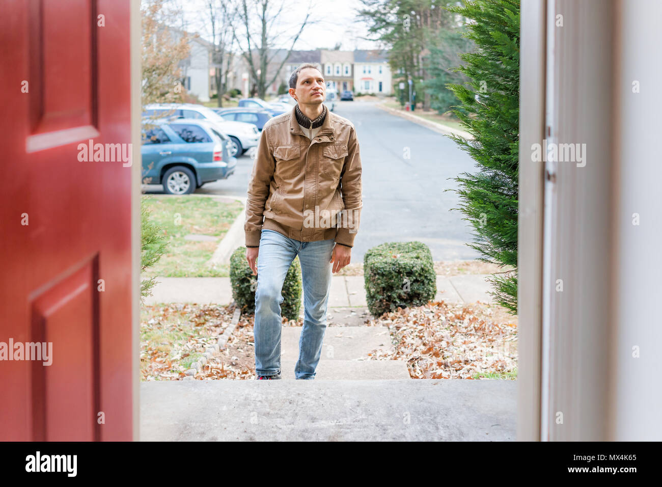 Young man standing on front porch frontyard steps in front of house home buyer looking to buy property real estate customer client in townhouse reside Stock Photo