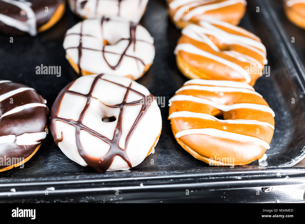 Chocolate brown, caramel, and white icing donuts with holes closeup on bakery tray, deep fried vanilla, delicious tasty Stock Photo
