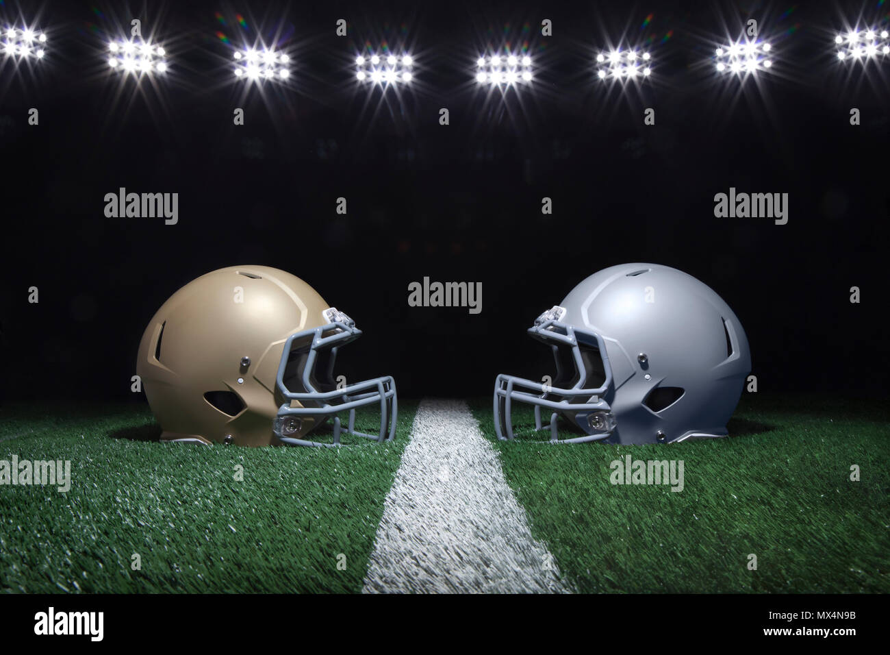 Gold and silver football helmets facing off on a yard line below stadium lights at night Stock Photo