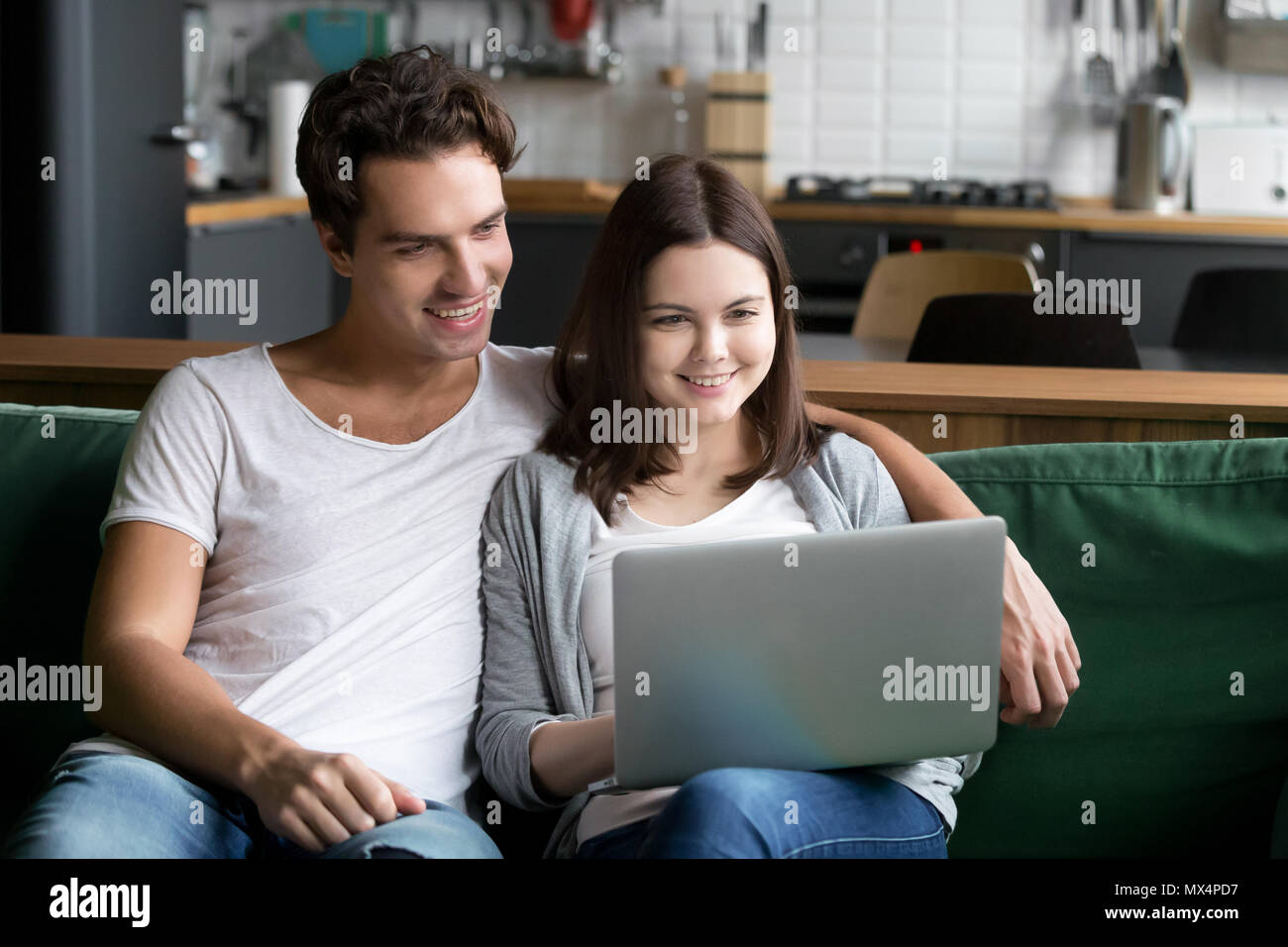 Smiling millennial couple using laptop computer sitting on kitch Stock Photo
