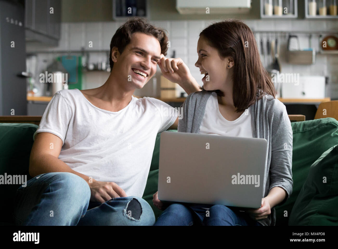 Happy millennial couple laughing using laptop together on kitche Stock Photo