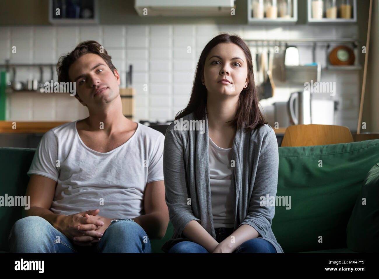 Lazy millennial couple getting bored at home sitting on sofa Stock Photo