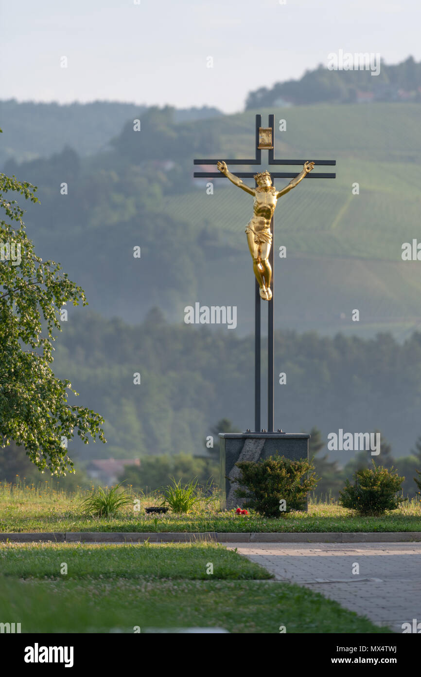 Jesus Christ on cross, golden statue against green natural background Stock Photo