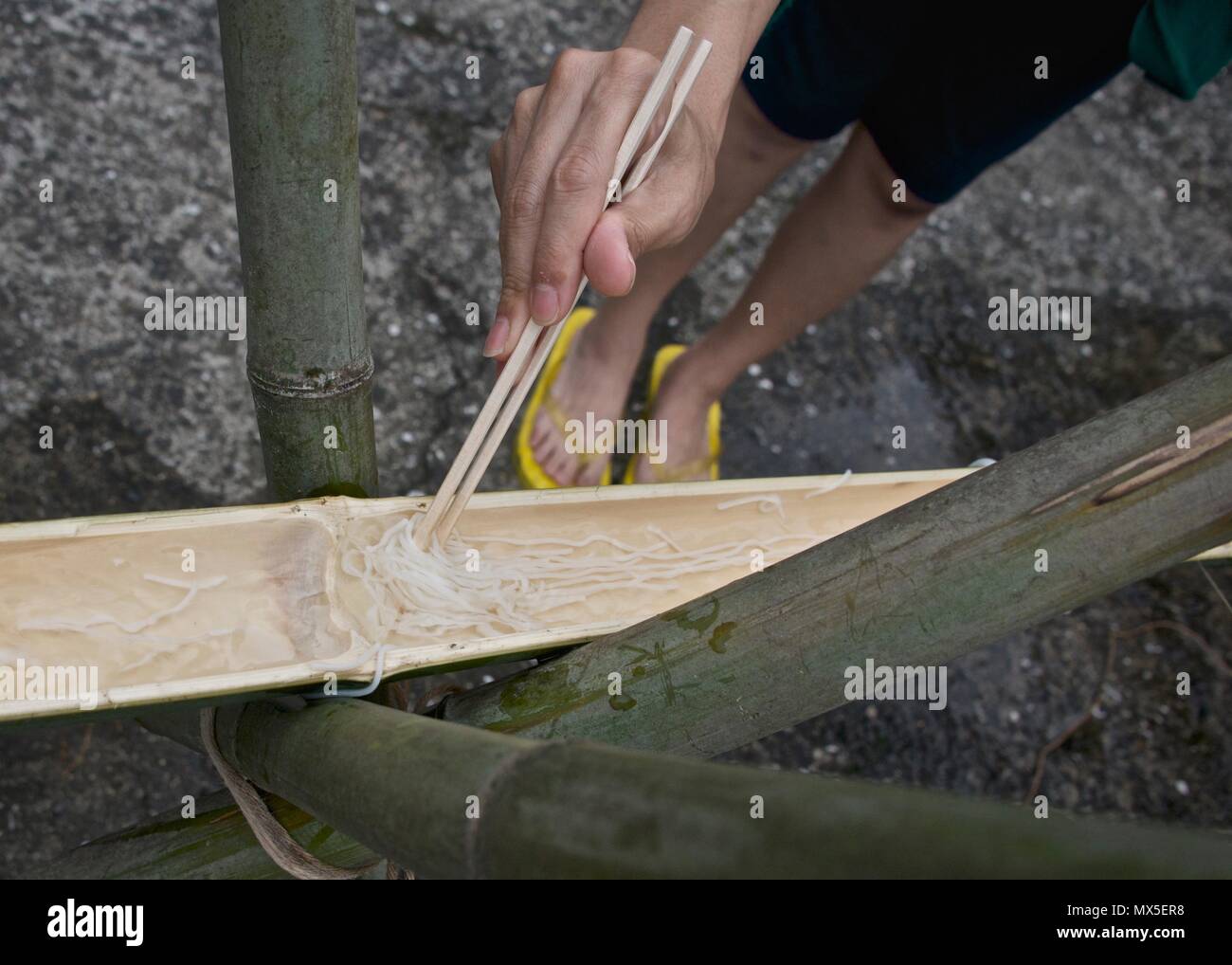Catching a flowing noodle while eating traditional nagashi suomen (flowing noodles) in Kyushu, Japan Stock Photo