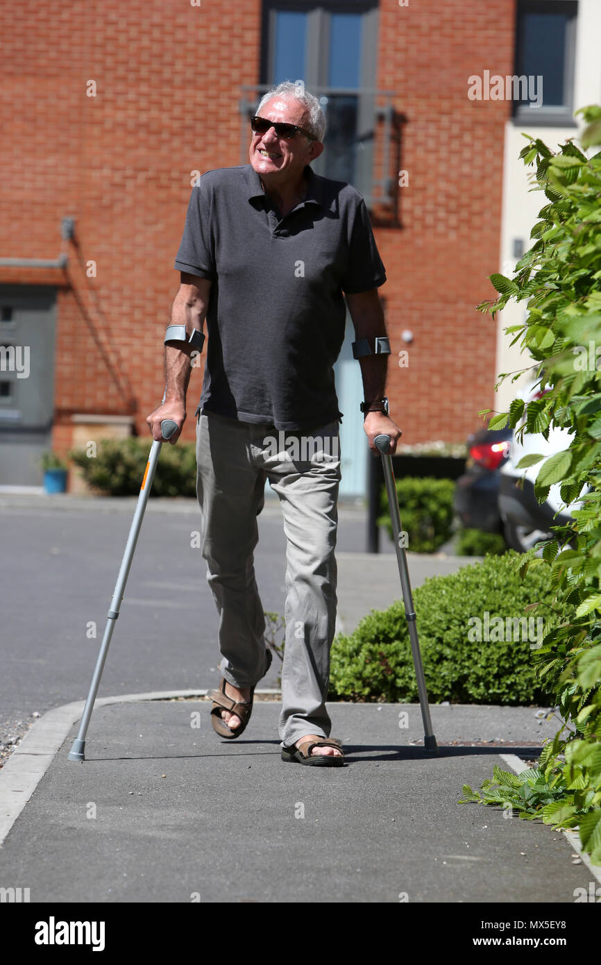 An older man pictured walking with crutches on a bad leg in Chichester, West Sussex, UK. Stock Photo