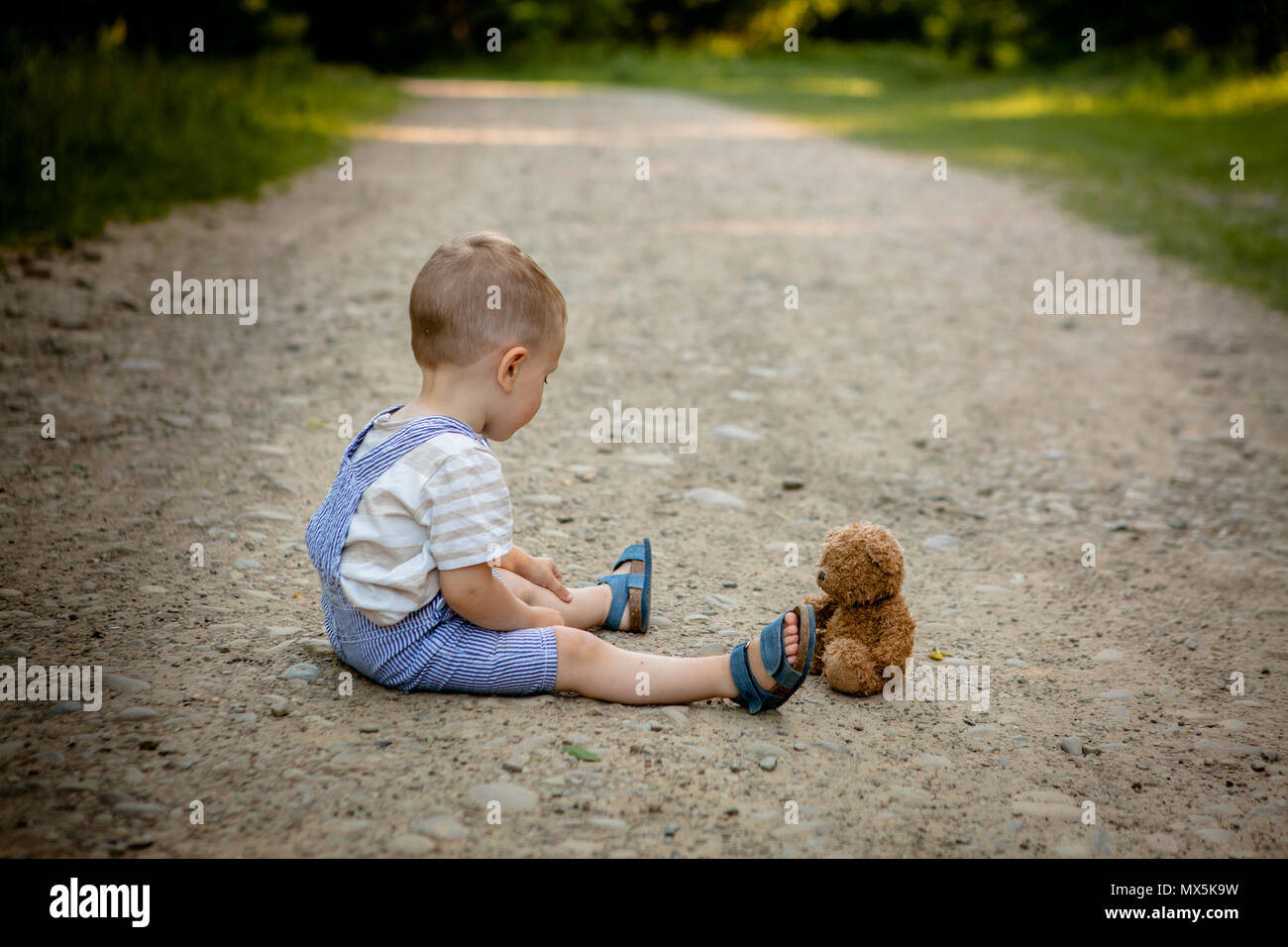 Little boy playing with teddy bear on the footpath Stock Photo - Alamy