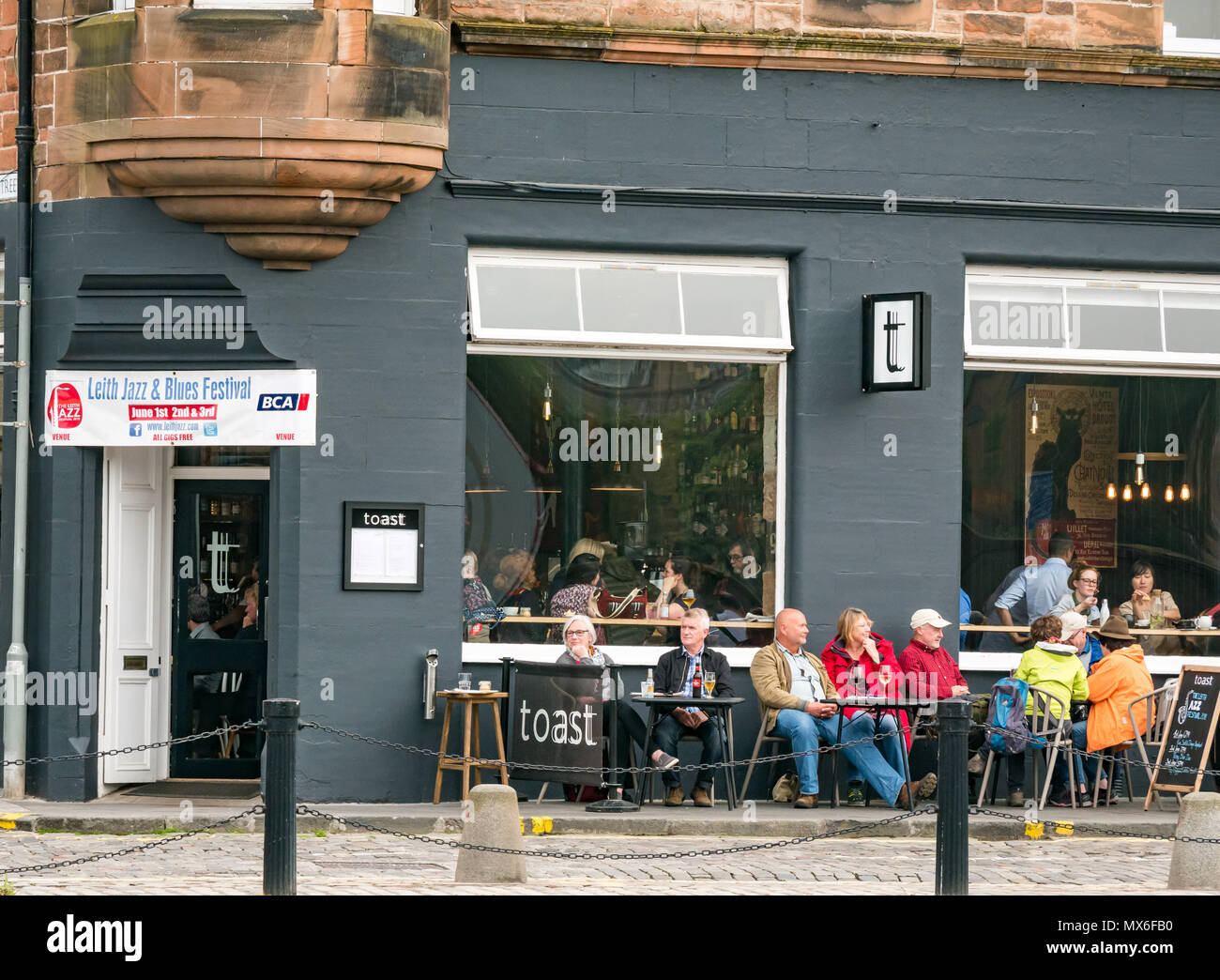 Leith Jazz & Blues Festival live music in restaurants and bars by the Water of  Leith, 3rd June 2018. The Shore, Leith, Edinburgh, Scotland, United Kingdom. The jazz and blues festival takes place over 3 weekend days. People throng the outdoor pavement tables of the restaurants and bars along the Water of Leith enjoying listening to the free live music. People at the wine bar and restaurant called Toast with the festival banner displayed Stock Photo