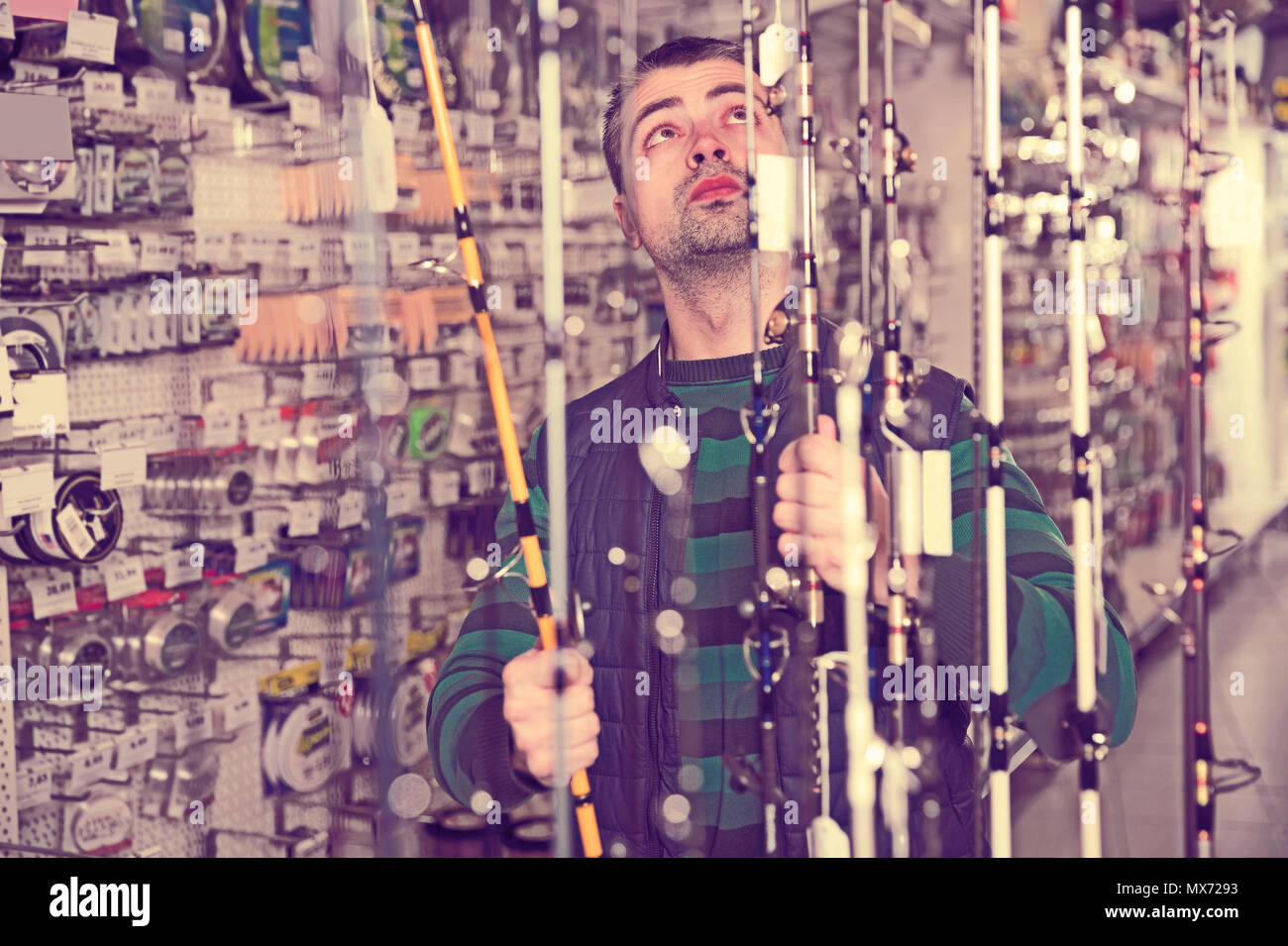 Young fisher choosing fishing rod in the sports shop indoors Stock Photo