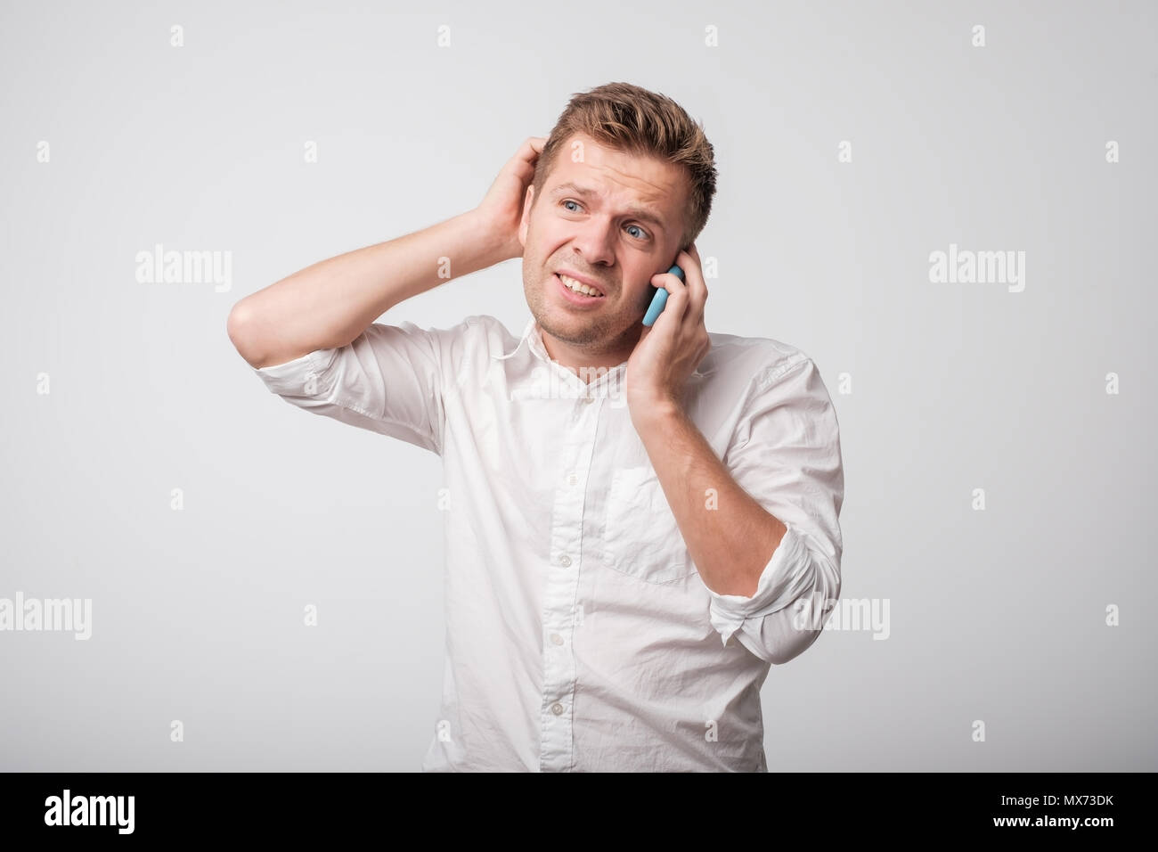Portrait of young caucasian uncertain man using mobile phone on gray background. Stock Photo