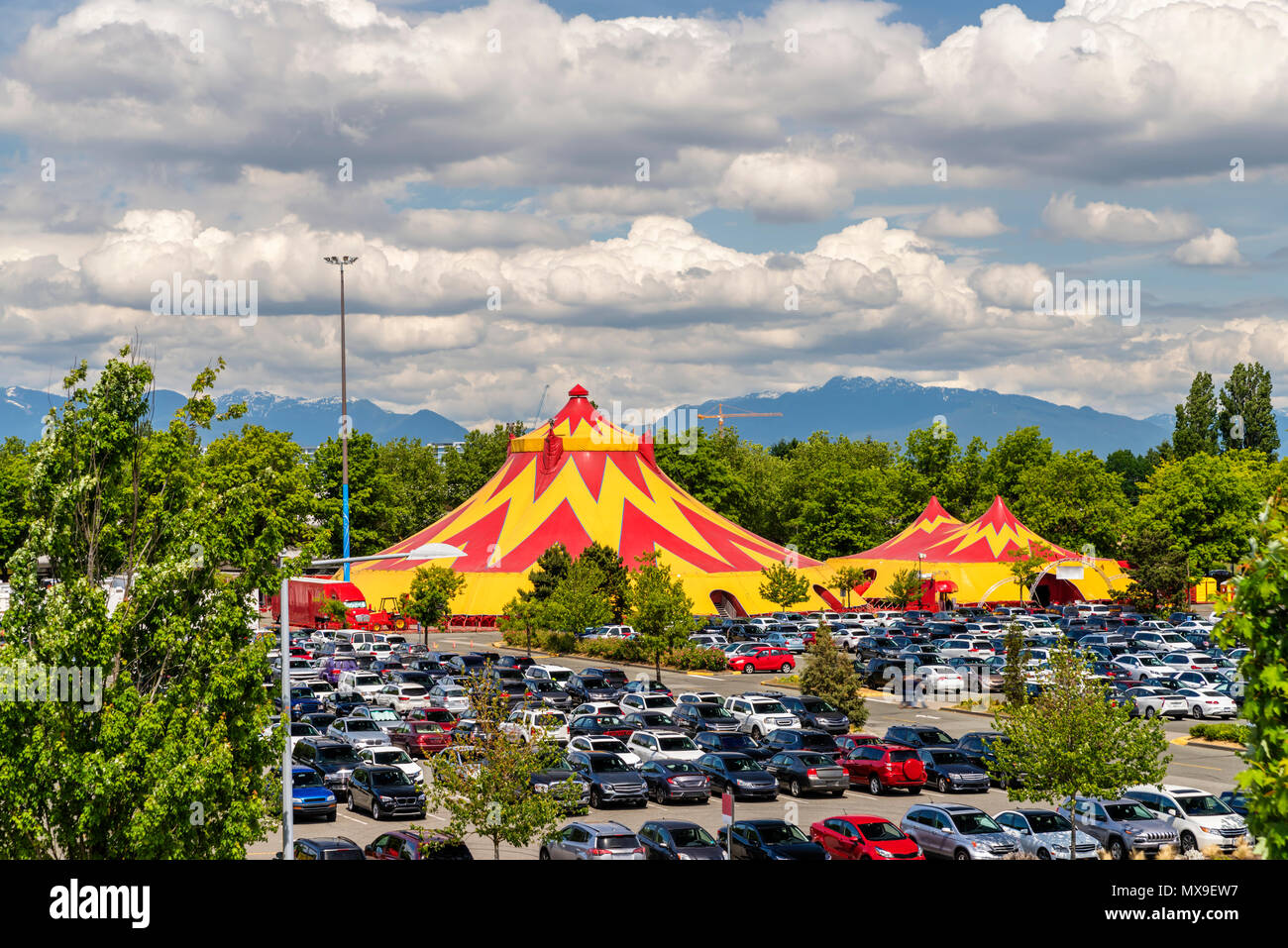 A mobile circus in the city, green trees and mountains in the distance, cars in a parking lot, a blue sky with dense clouds on a summer day Stock Photo