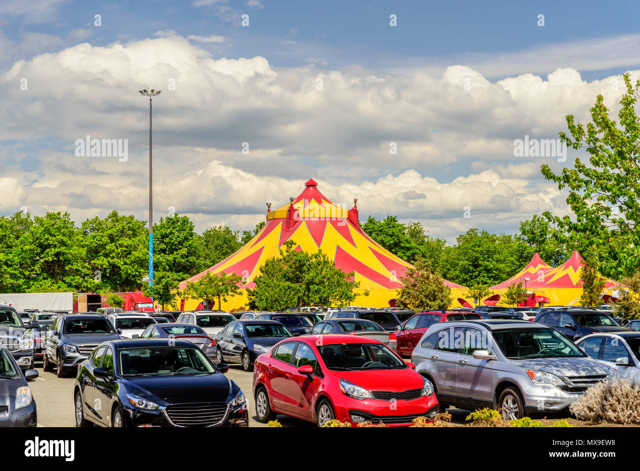 Domes of a caravan circus in the city, green trees, cars in a parking lot, a blue sky with dense clouds on a summer day Stock Photo