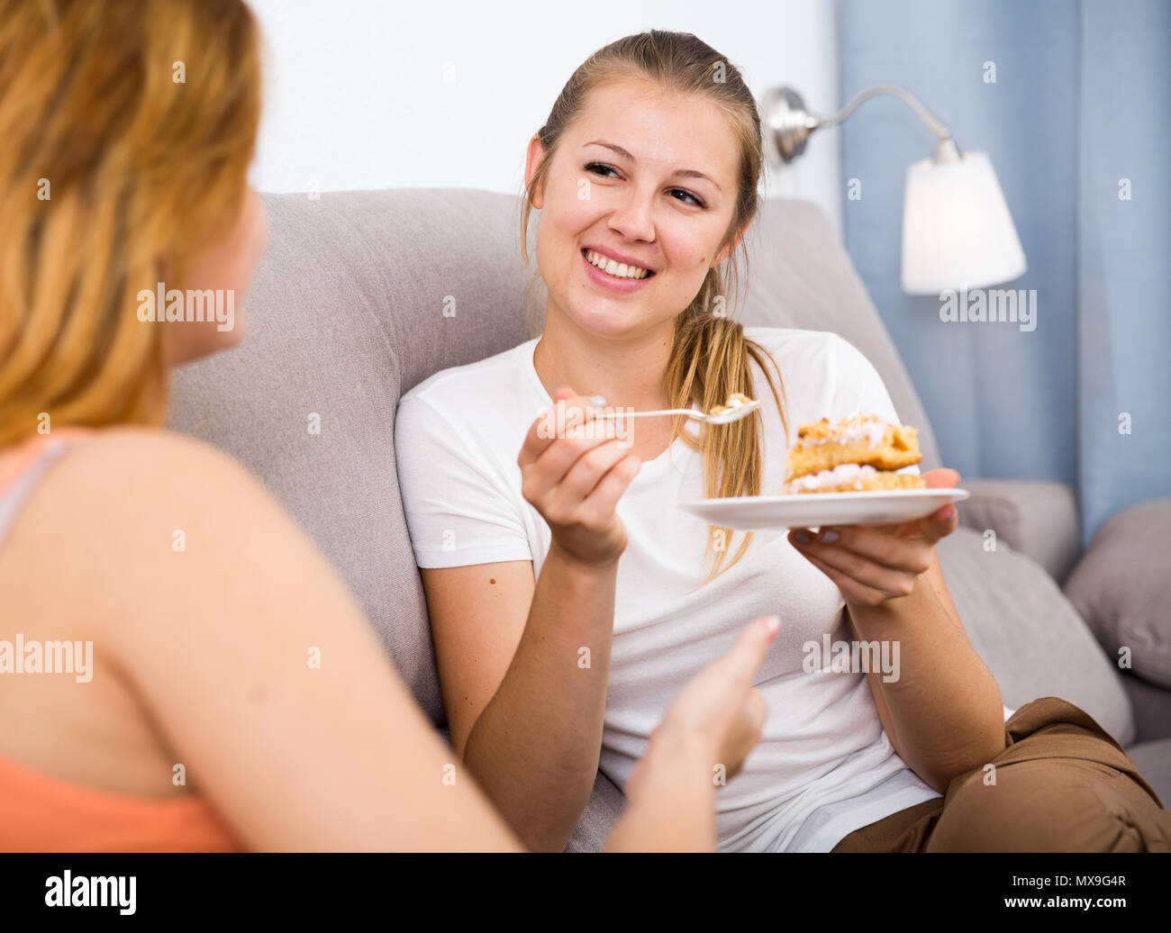 Smiling young friends eating sweet pie on cozy sofa at home Stock Photo. 