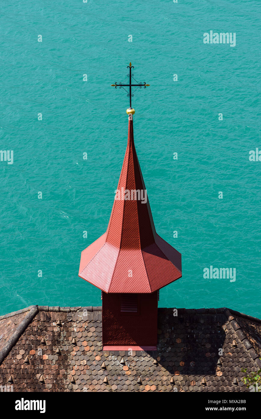 Minimalistic shot of the top of Catholic chapel roof spire cross over Lake Lucerne turquoise waters on summer spring clear day Stock Photo