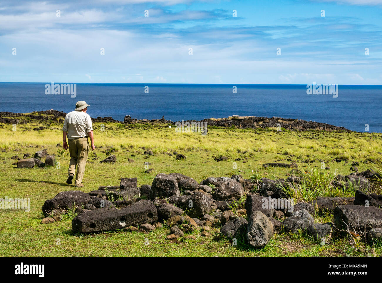 Senior male tourist in khaki clothing walking among remains of traditional stone village houses, Te Peu, Easter Island, Rapa Nui, Chile Stock Photo