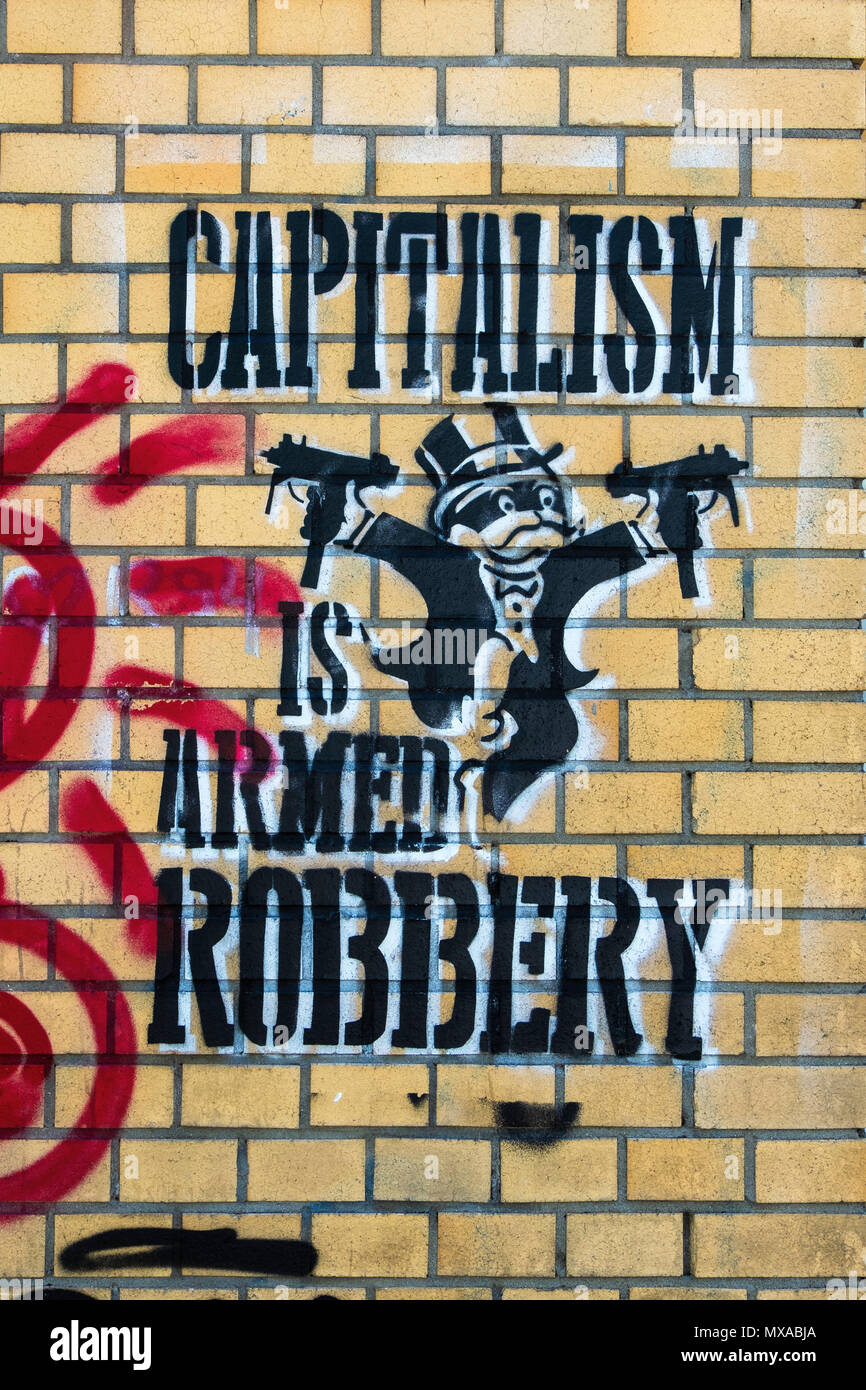 Street art stencil on Brick wall with political slogan - Capitalism is Armed Robbery, Berlin, Germany Stock Photo