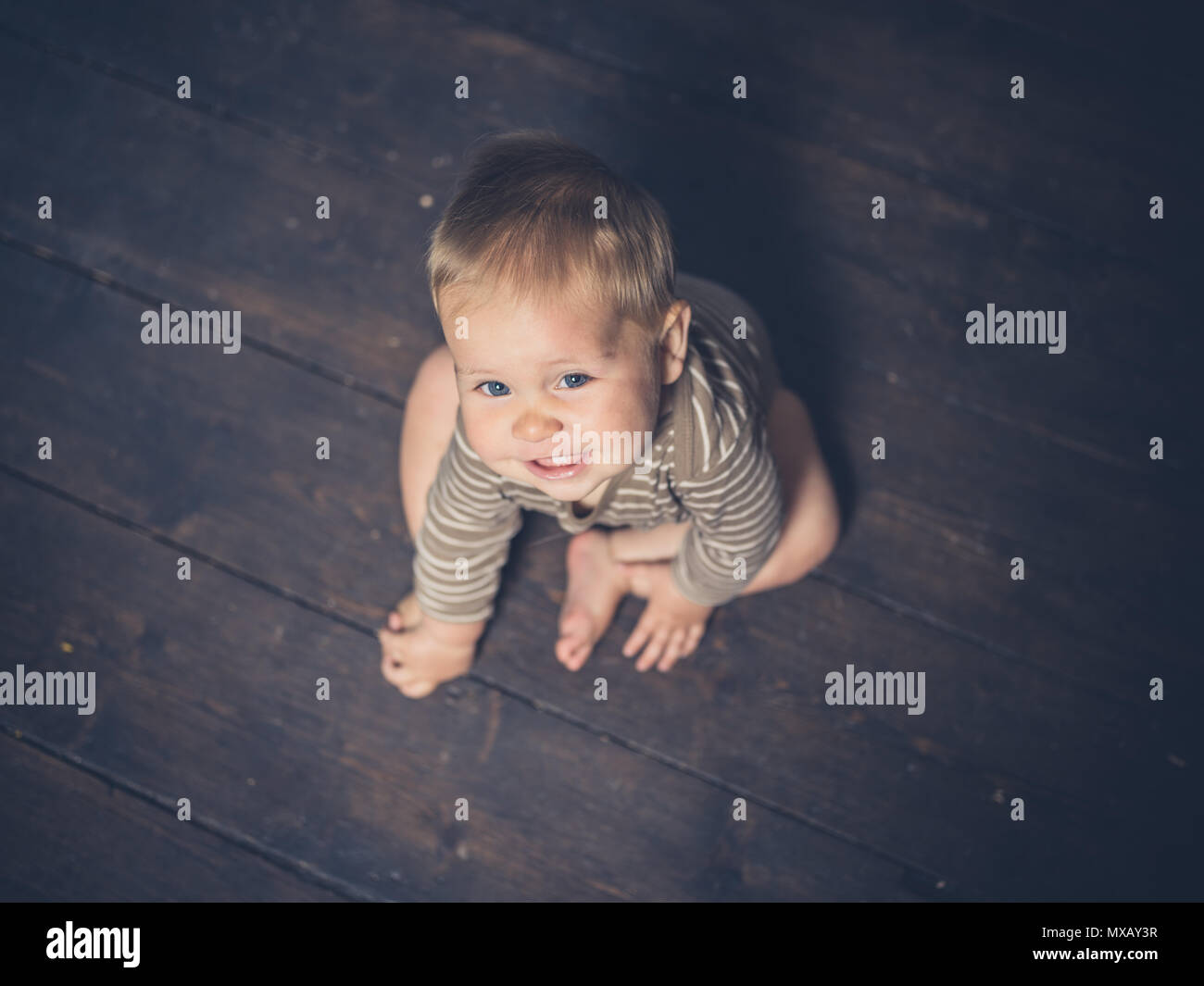 A little baby is sitting on the floorboards looking up Stock Photo Alamy