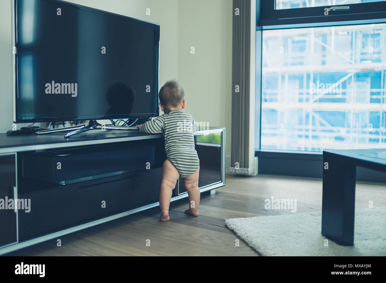 A cute little baby is crusing on the television furniture in a city